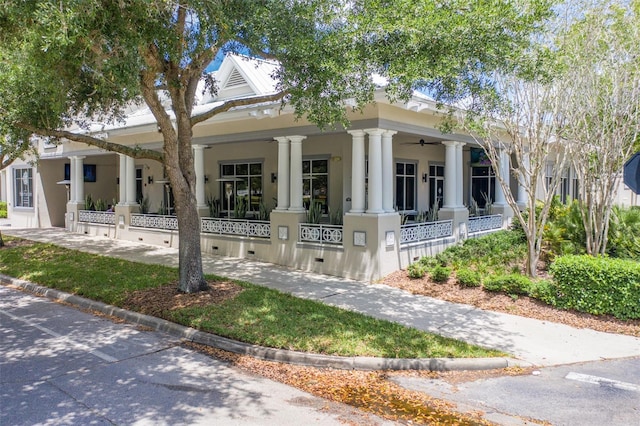 greek revival house featuring covered porch, a ceiling fan, and stucco siding