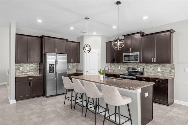 kitchen with hanging light fixtures, stainless steel appliances, a center island with sink, sink, and a kitchen bar