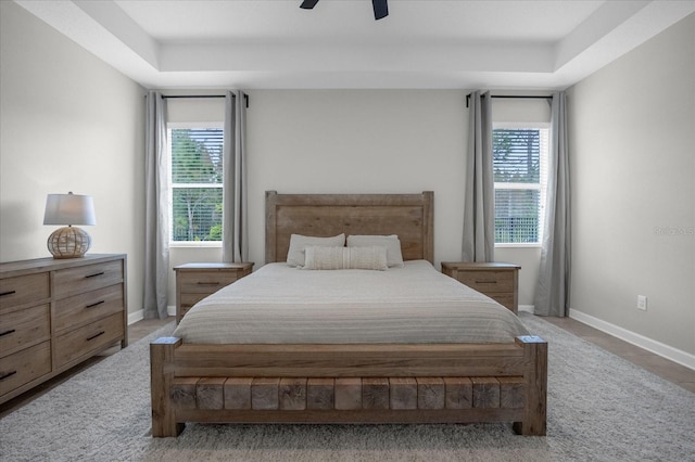 bedroom featuring multiple windows, a tray ceiling, and ceiling fan