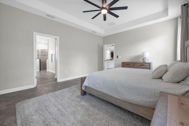 bedroom featuring a raised ceiling, ensuite bathroom, and ceiling fan