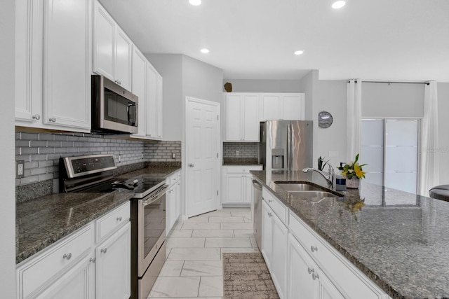 kitchen with white cabinets, backsplash, dark stone countertops, sink, and stainless steel appliances