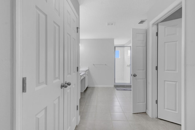 hall with a textured ceiling and light tile patterned floors