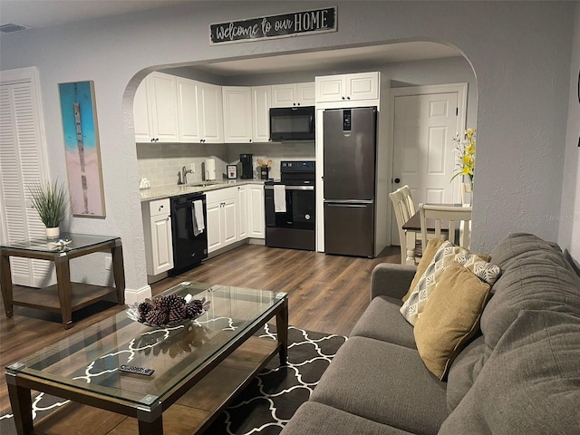 interior space with dark wood-style flooring, arched walkways, black appliances, and light countertops