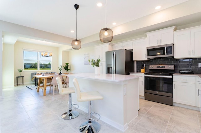 kitchen with a kitchen island, backsplash, white cabinets, decorative light fixtures, and appliances with stainless steel finishes