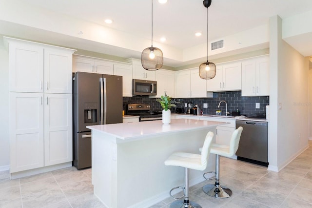 kitchen featuring tasteful backsplash, appliances with stainless steel finishes, white cabinetry, decorative light fixtures, and a center island