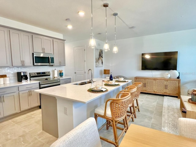 kitchen with appliances with stainless steel finishes, a sink, gray cabinets, a breakfast bar, and tasteful backsplash