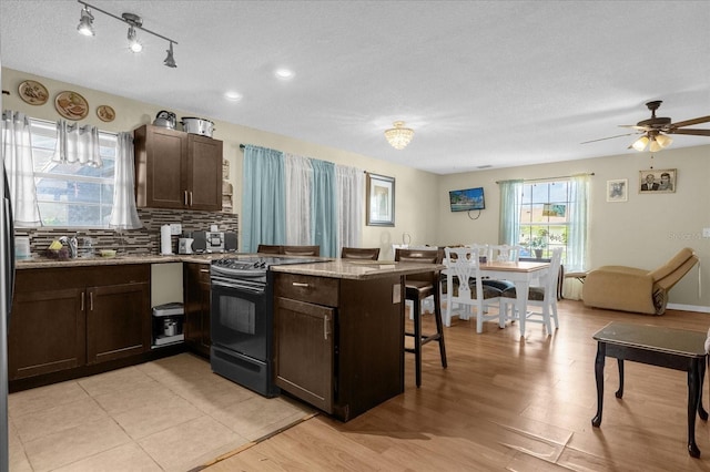 kitchen with black range with electric cooktop, a breakfast bar, kitchen peninsula, and light wood-type flooring