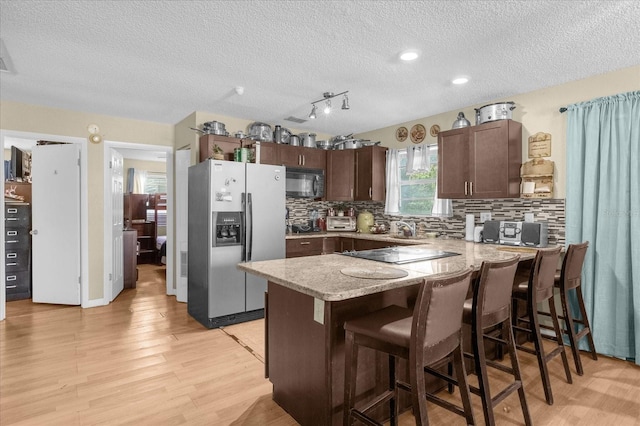 kitchen featuring a breakfast bar area, stainless steel refrigerator with ice dispenser, dark brown cabinetry, a textured ceiling, and light hardwood / wood-style floors