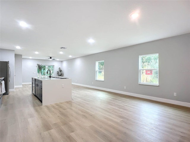 kitchen with sink, stainless steel fridge, ceiling fan, light hardwood / wood-style floors, and a kitchen island with sink