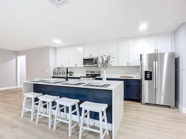 kitchen with a breakfast bar, appliances with stainless steel finishes, light hardwood / wood-style flooring, and white cabinets