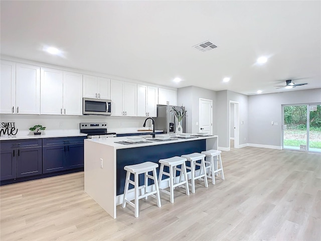 kitchen featuring appliances with stainless steel finishes, white cabinets, a center island with sink, and light hardwood / wood-style floors