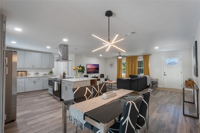 dining room with light wood-type flooring, ceiling fan with notable chandelier, and a textured ceiling