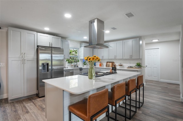 kitchen featuring stainless steel appliances, a breakfast bar area, island range hood, a kitchen island, and dark wood-type flooring