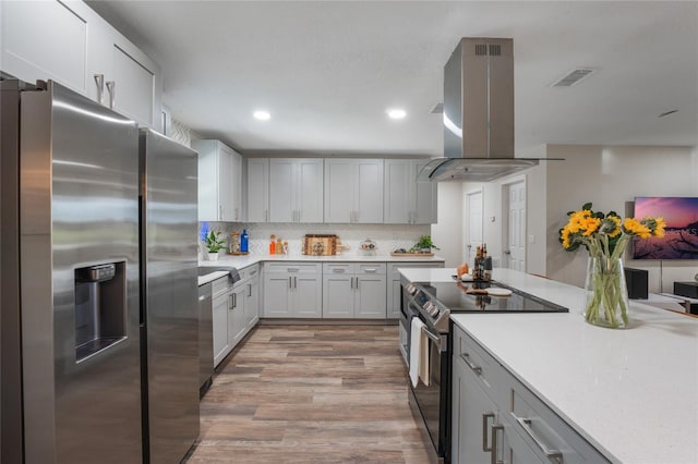 kitchen featuring light hardwood / wood-style floors, gray cabinets, island exhaust hood, backsplash, and appliances with stainless steel finishes