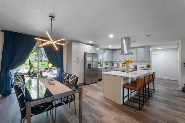 kitchen with island range hood, wood-type flooring, a kitchen island, backsplash, and stainless steel refrigerator with ice dispenser