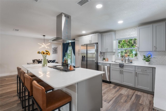 kitchen with stainless steel appliances, dark hardwood / wood-style floors, decorative light fixtures, island exhaust hood, and gray cabinetry