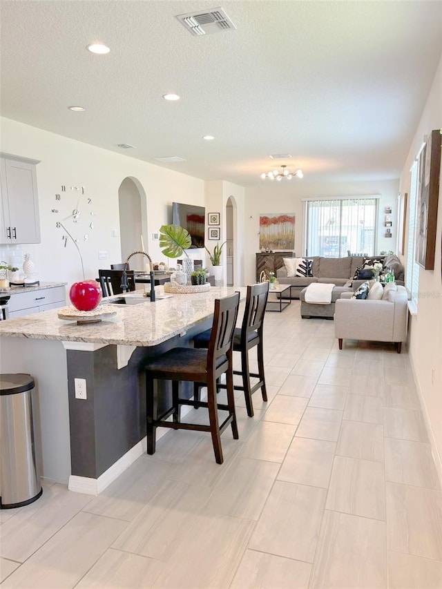 kitchen with a breakfast bar area, an island with sink, sink, light stone counters, and a textured ceiling