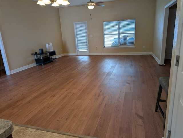 unfurnished living room featuring ceiling fan with notable chandelier and hardwood / wood-style flooring