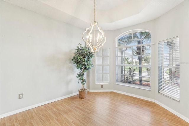 empty room with a wealth of natural light, hardwood / wood-style flooring, and an inviting chandelier