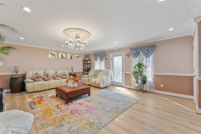 living room with an inviting chandelier, light hardwood / wood-style flooring, a textured ceiling, and crown molding