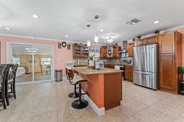 kitchen with a kitchen island, wall chimney exhaust hood, a breakfast bar area, hanging light fixtures, and appliances with stainless steel finishes