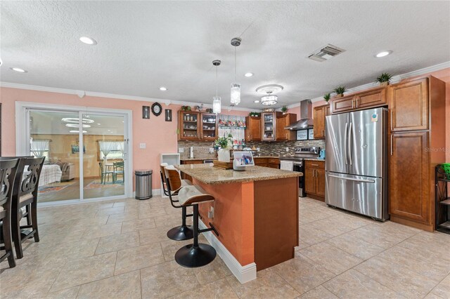 1395 Emerald Dr, Kissimmee, FL 34744 - kitchen with stainless steel appliances, wall chimney range hood, brown cabinets, crown molding, and tasteful backsplash