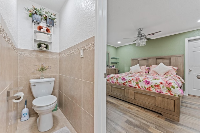 bathroom featuring toilet, hardwood / wood-style floors, tile walls, and ceiling fan