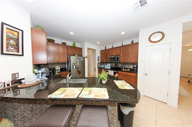 kitchen with tasteful backsplash, appliances with stainless steel finishes, light tile patterned flooring, kitchen peninsula, and a breakfast bar area