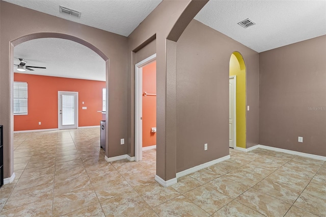 unfurnished room with a ceiling fan, arched walkways, visible vents, and a textured ceiling