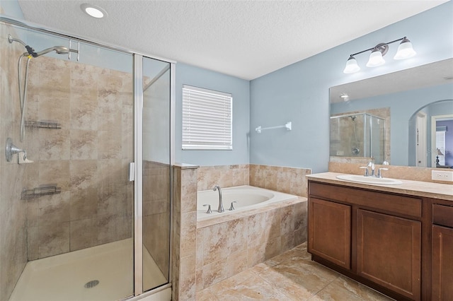 bathroom with a shower stall, a textured ceiling, a bath, and vanity