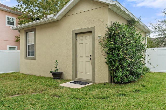 view of exterior entry featuring stucco siding, a yard, and fence