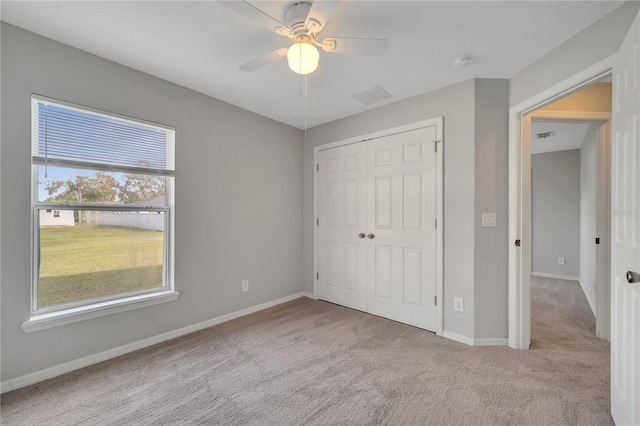 unfurnished bedroom featuring light colored carpet, multiple windows, ceiling fan, and a closet