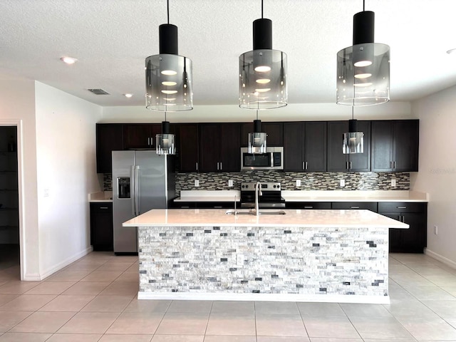 kitchen with decorative light fixtures, stainless steel appliances, a kitchen island with sink, and sink