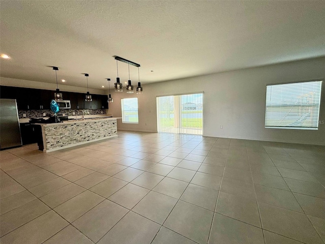 kitchen with appliances with stainless steel finishes, backsplash, pendant lighting, an island with sink, and light tile patterned flooring