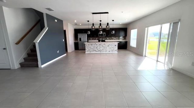 kitchen with hanging light fixtures, light tile patterned floors, an island with sink, and appliances with stainless steel finishes