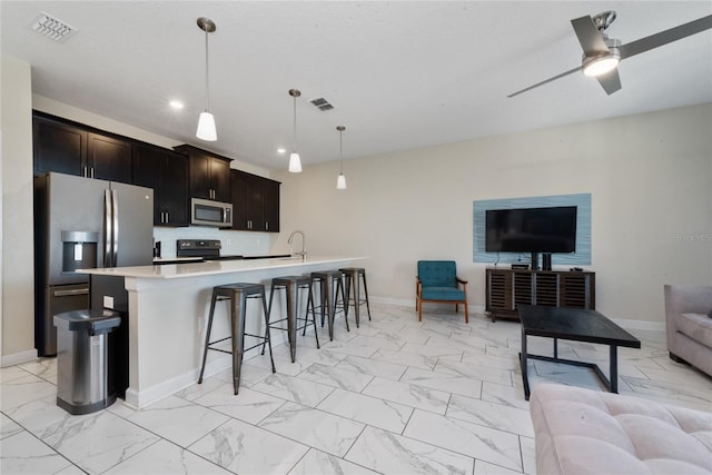 kitchen featuring ceiling fan, a kitchen island with sink, sink, pendant lighting, and stainless steel appliances