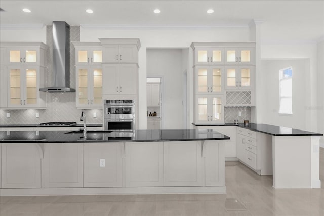 kitchen featuring wall chimney range hood, crown molding, white cabinetry, and stainless steel appliances