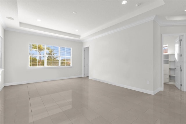 empty room with light tile patterned floors, ornamental molding, and a tray ceiling