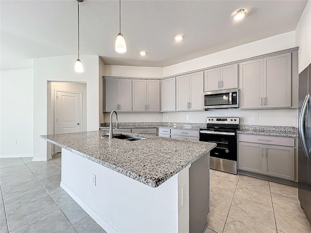 kitchen featuring an island with sink, hanging light fixtures, stainless steel appliances, dark stone counters, and sink