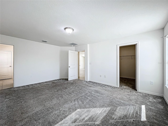 unfurnished bedroom with a walk in closet, a textured ceiling, a closet, and dark carpet