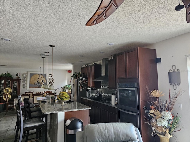 kitchen featuring a breakfast bar area, stainless steel appliances, a kitchen island with sink, wall chimney exhaust hood, and light stone counters