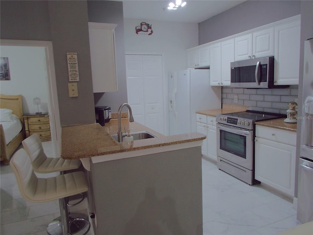 kitchen with decorative backsplash, a breakfast bar area, stainless steel appliances, sink, and white cabinetry