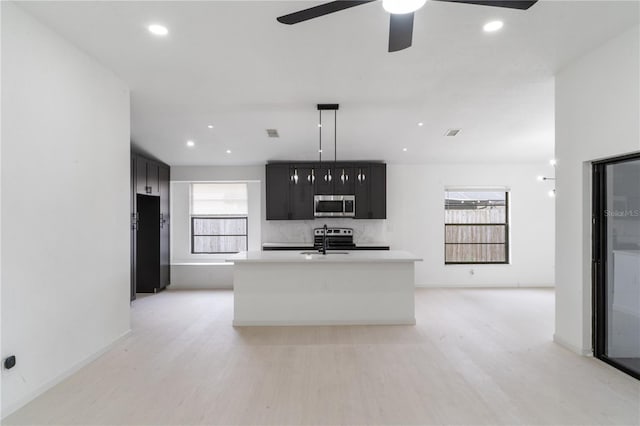 kitchen with decorative light fixtures, sink, light hardwood / wood-style floors, stainless steel appliances, and a center island with sink