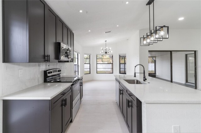 kitchen with sink, tasteful backsplash, hanging light fixtures, appliances with stainless steel finishes, and light stone countertops