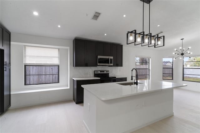 kitchen with sink, a kitchen island with sink, pendant lighting, and electric stove