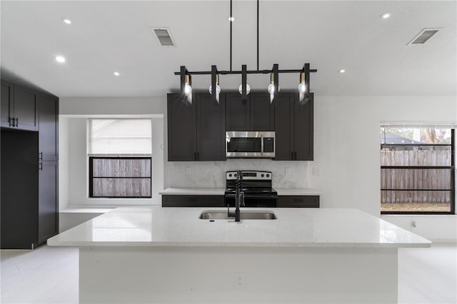 kitchen with pendant lighting, electric range, a kitchen island with sink, and light stone countertops