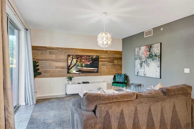 living room featuring a notable chandelier, light tile patterned flooring, and wood walls