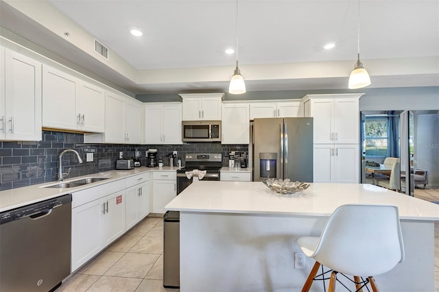 kitchen featuring appliances with stainless steel finishes, white cabinetry, sink, pendant lighting, and a center island