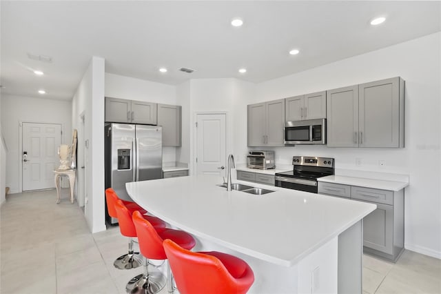 kitchen featuring sink, a breakfast bar area, gray cabinets, an island with sink, and stainless steel appliances