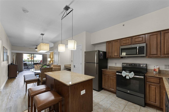 kitchen featuring light stone counters, a breakfast bar area, appliances with stainless steel finishes, light hardwood / wood-style flooring, and a center island